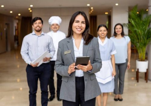 Adherence to Hospitality Standards Happy Latin American hotel manager leading a group of employees at the lobby and looking at the camera smiling